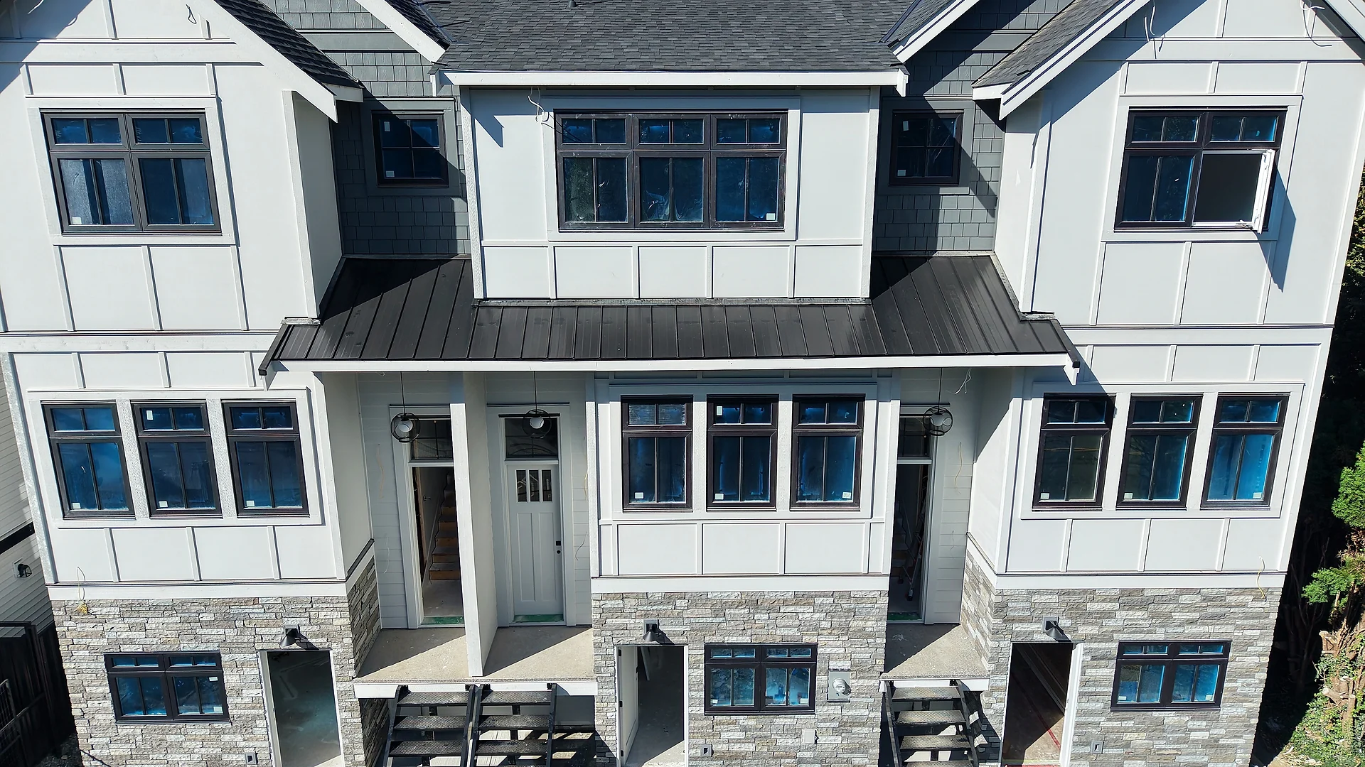 Three-storey townhouse block in white board and batten and panel over a stone base, seen from the air, Abbotsford BC — siding by Moonrise Construction