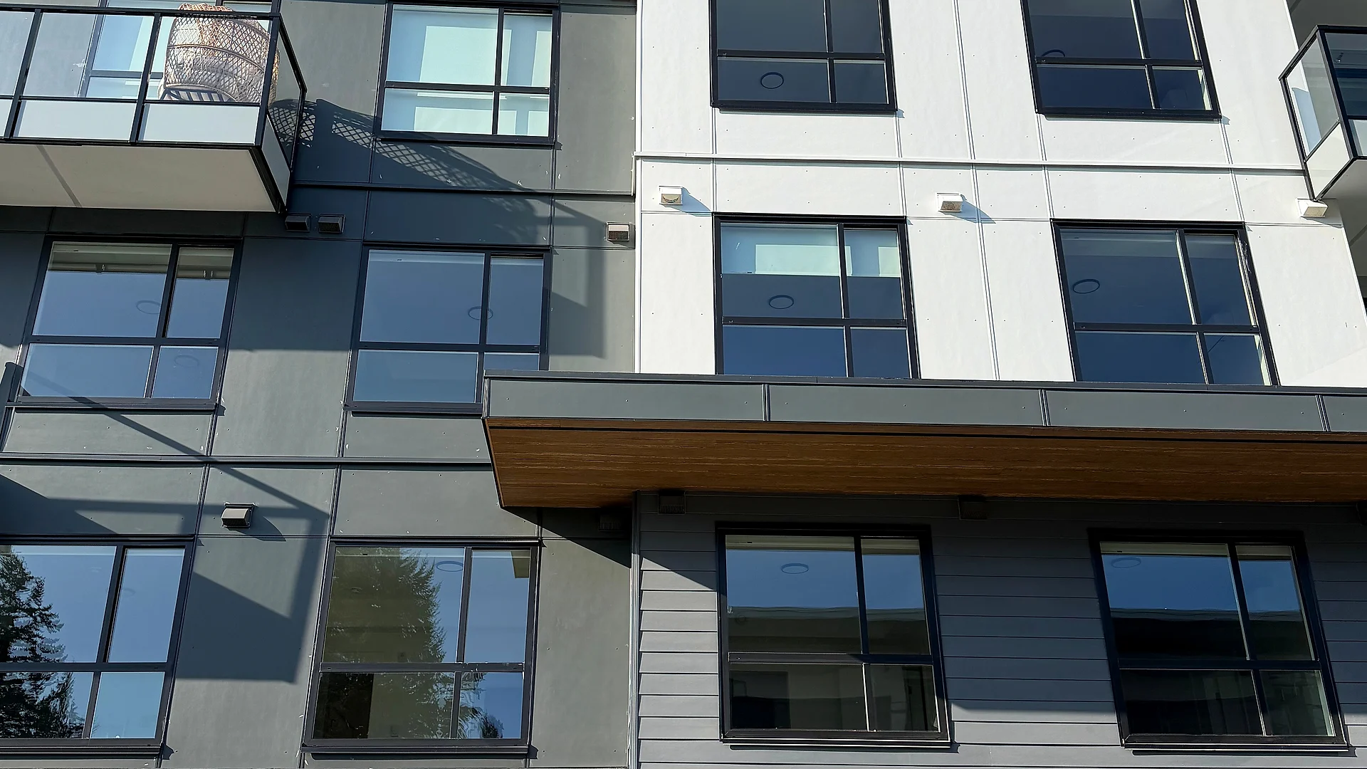 Four-storey mid-rise straight-on, grey lap siding, white panel and glass balconies, South Surrey BC — exterior finishing by Moonrise Construction